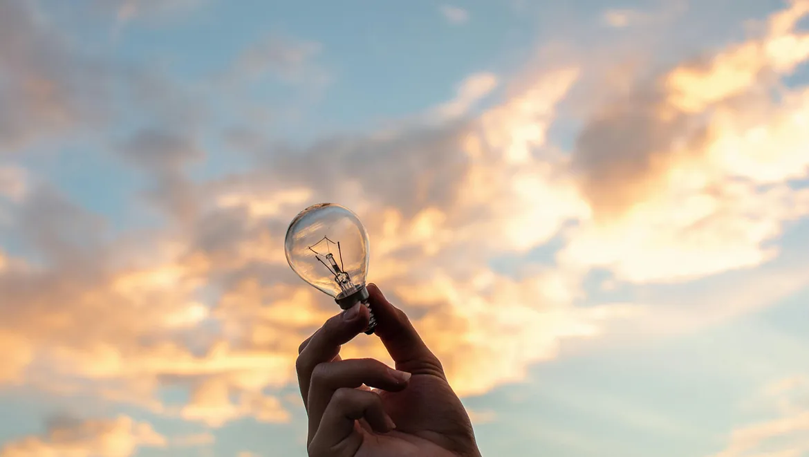 hand håller glödlampa mot himlen